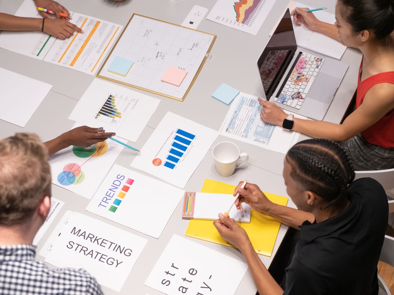 Vue aérienne d’une équipe variée analysant des stratégies marketing à l’aide de graphiques et de schémas.